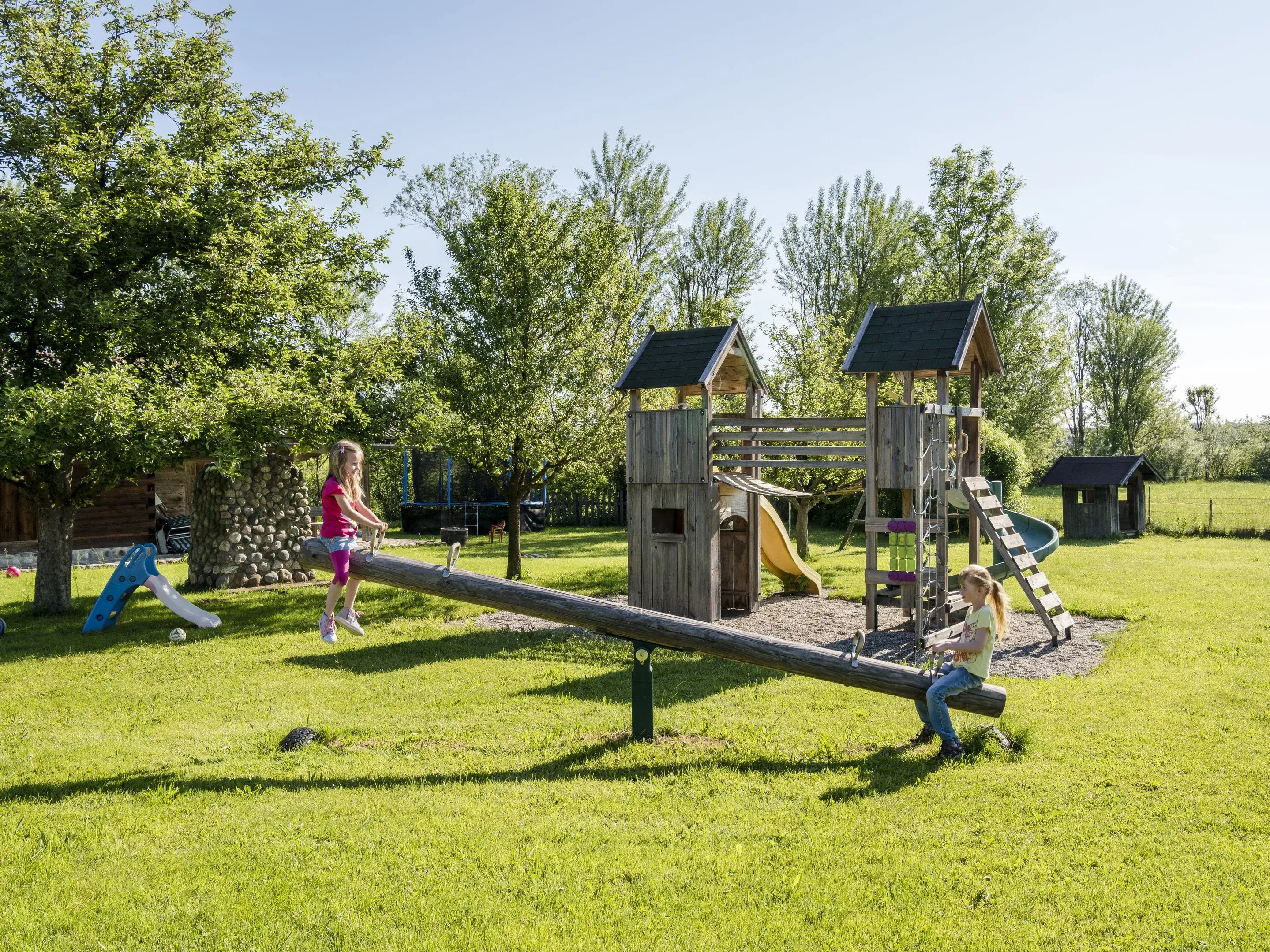 Kinder schauckeln auf dem Kinderspielplatz auf dem Urlaubsbauernhof Kinder sind auf dem Kinderspielplatz am spielen und sitzen auf einer Schaukel auf dem Urlaubsbauernhof